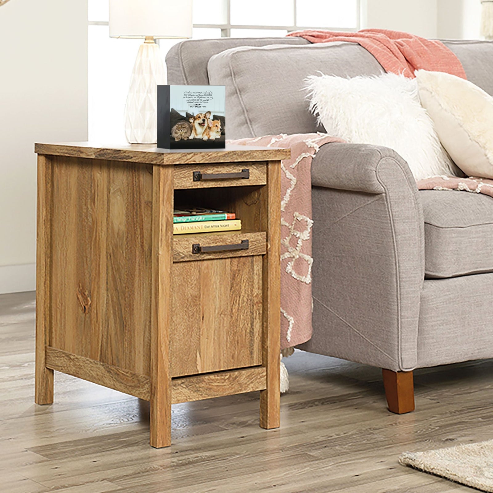 Personalized pet photo urn shadow box, elegantly placed on a side table next to a gray couch in a modern living room. This wooden pet urn for ashes doubles as a sympathy gift for the loss of a pet and a shadow box memorial to honor beloved pets.