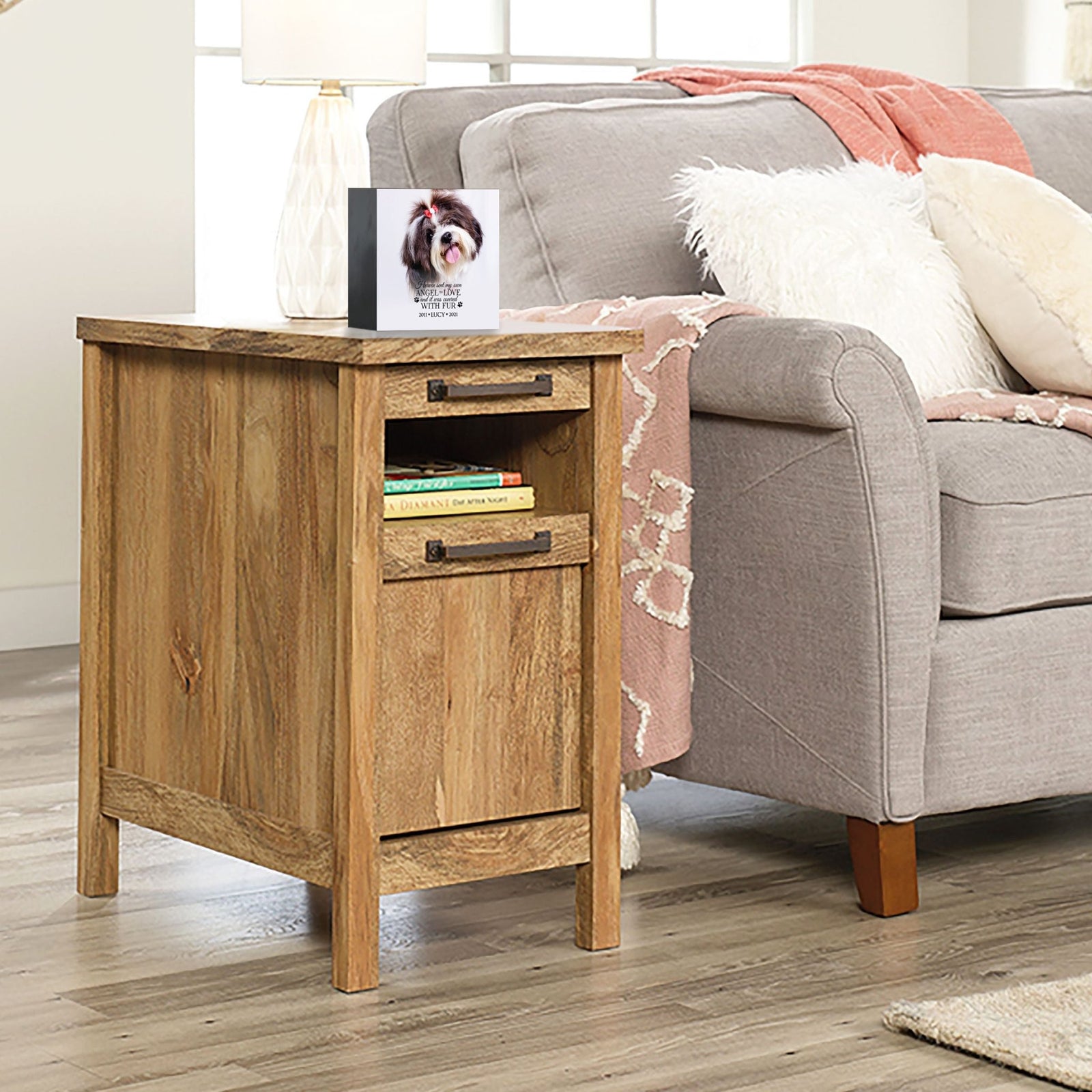 A personalized pet urn placed on a wooden side table beside a cozy gray couch.