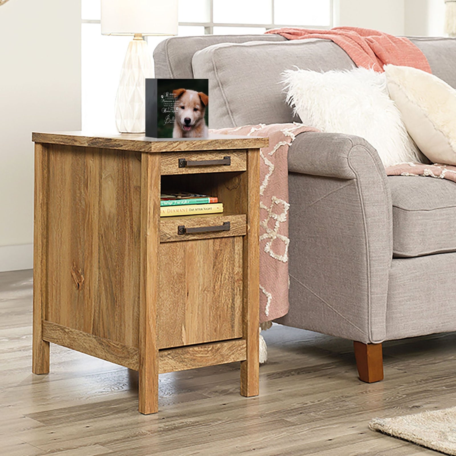 A personalized pet urn placed on a wooden side table beside a cozy gray couch.