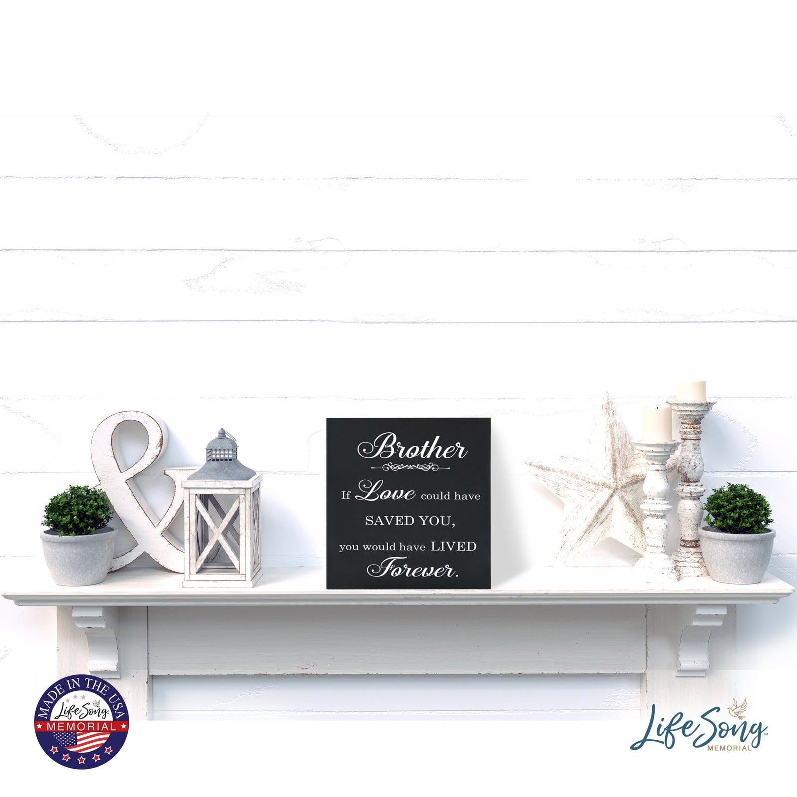 A decorative white shelf showcases a LifeSong Milestones Memorial Shadow Box Urn for human ashes, adorned with delightful accents such as lanterns, greenery, and star-shaped decorations. The urn features heartfelt engraving, fostering a serene and comforting ambiance.