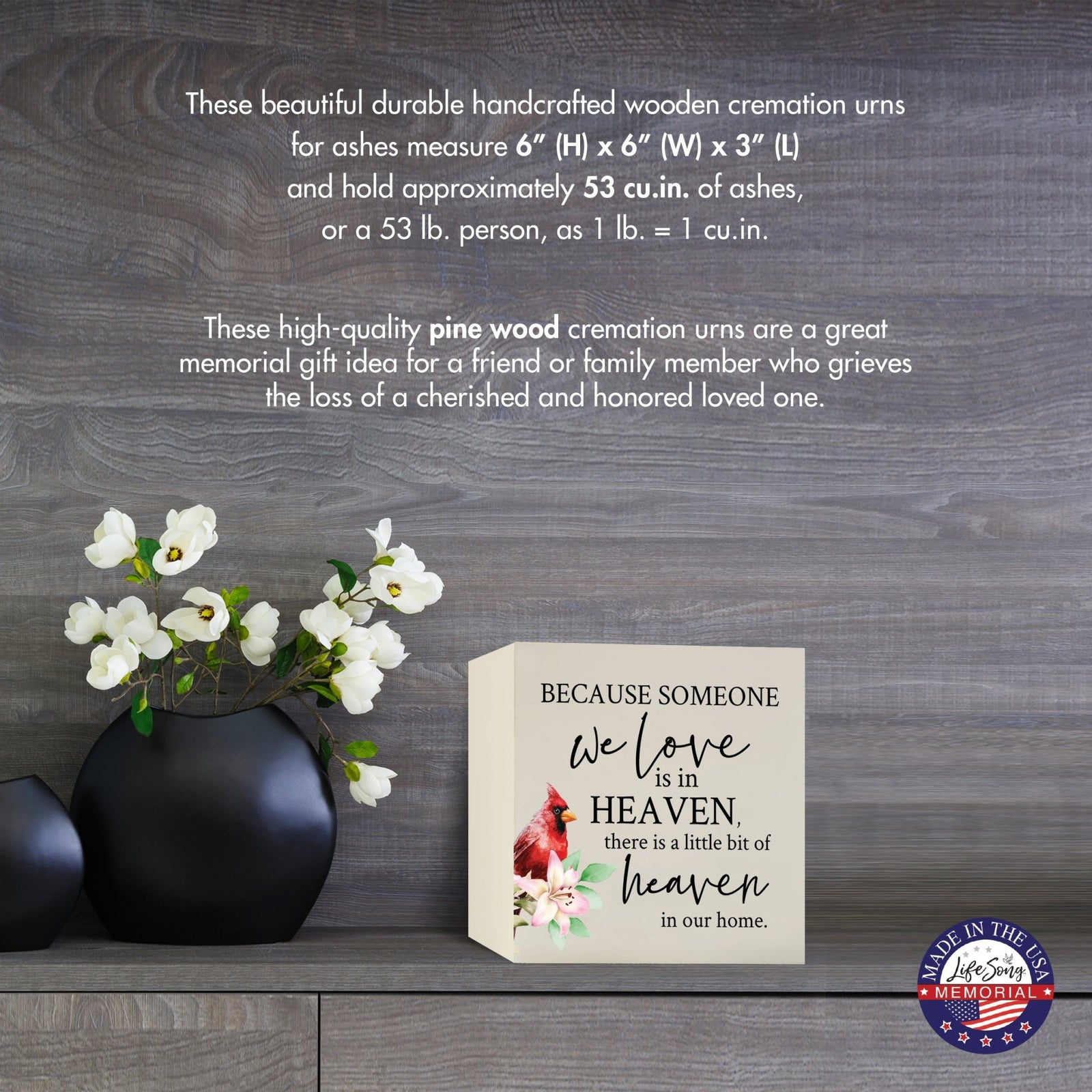 Cream-colored wooden shadow box urn for human ashes, measuring 6" x 6" x 3". The urn features a red cardinal and delicate floral design. Displayed on a wooden surface beside modern black vases with white flowers, this handcrafted urn is ideal for honoring adult loved ones.