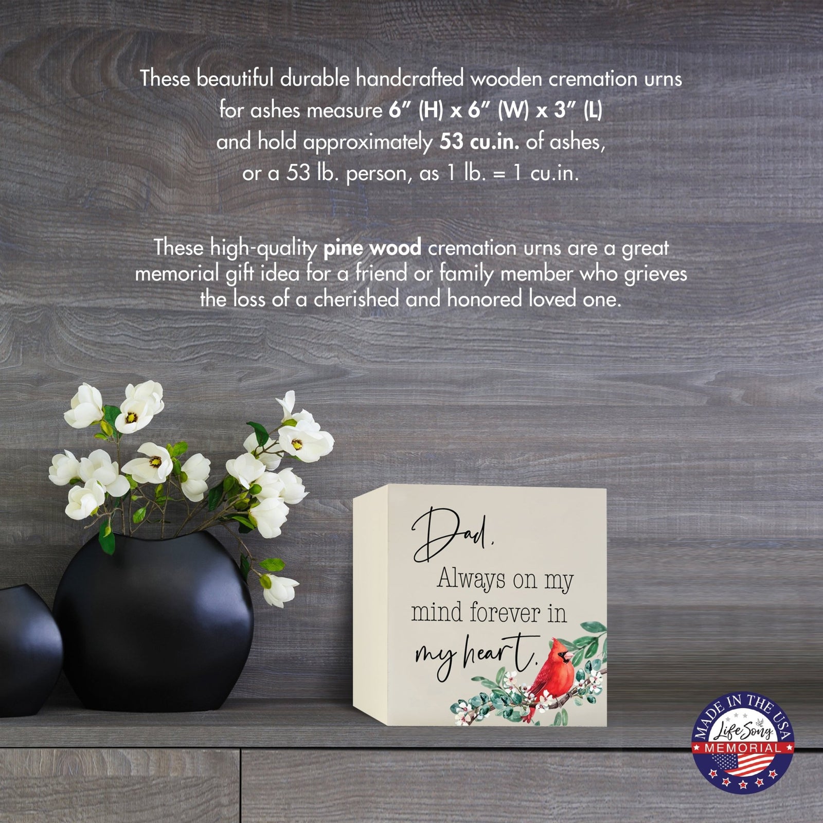 Cream-colored wooden shadow box urn for human ashes, measuring 6" x 6" x 3". The urn features a red cardinal and delicate floral design. Displayed on a wooden surface beside modern black vases with white flowers, this handcrafted urn is ideal for honoring adult loved ones.