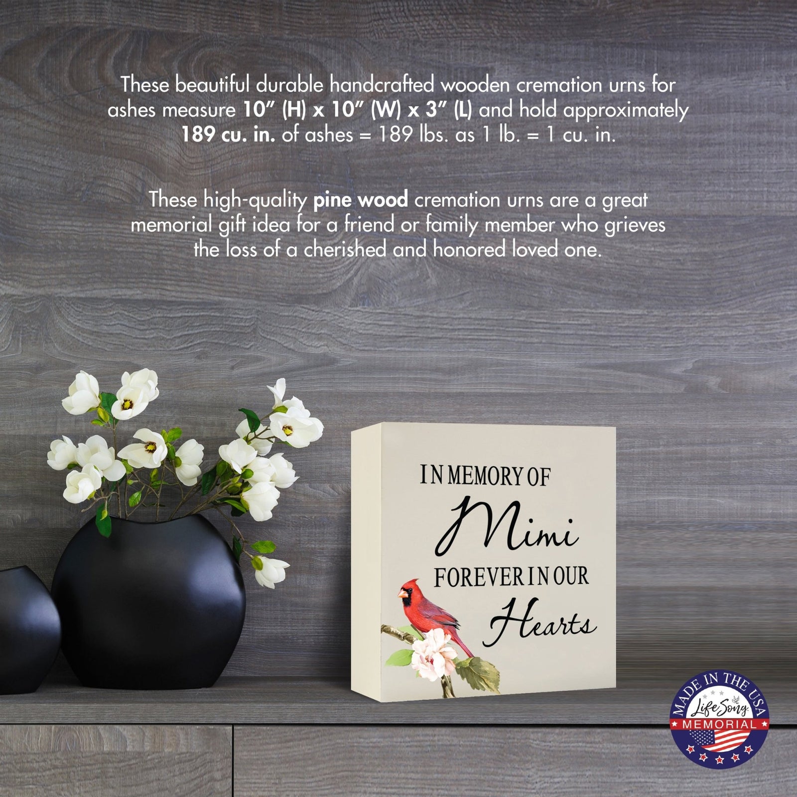 Cream-colored wooden shadow box urn for human ashes, measuring 6" x 6" x 3". The urn features a red cardinal and delicate floral design. Displayed on a wooden surface beside modern black vases with white flowers, this handcrafted urn is ideal for honoring adult loved ones.