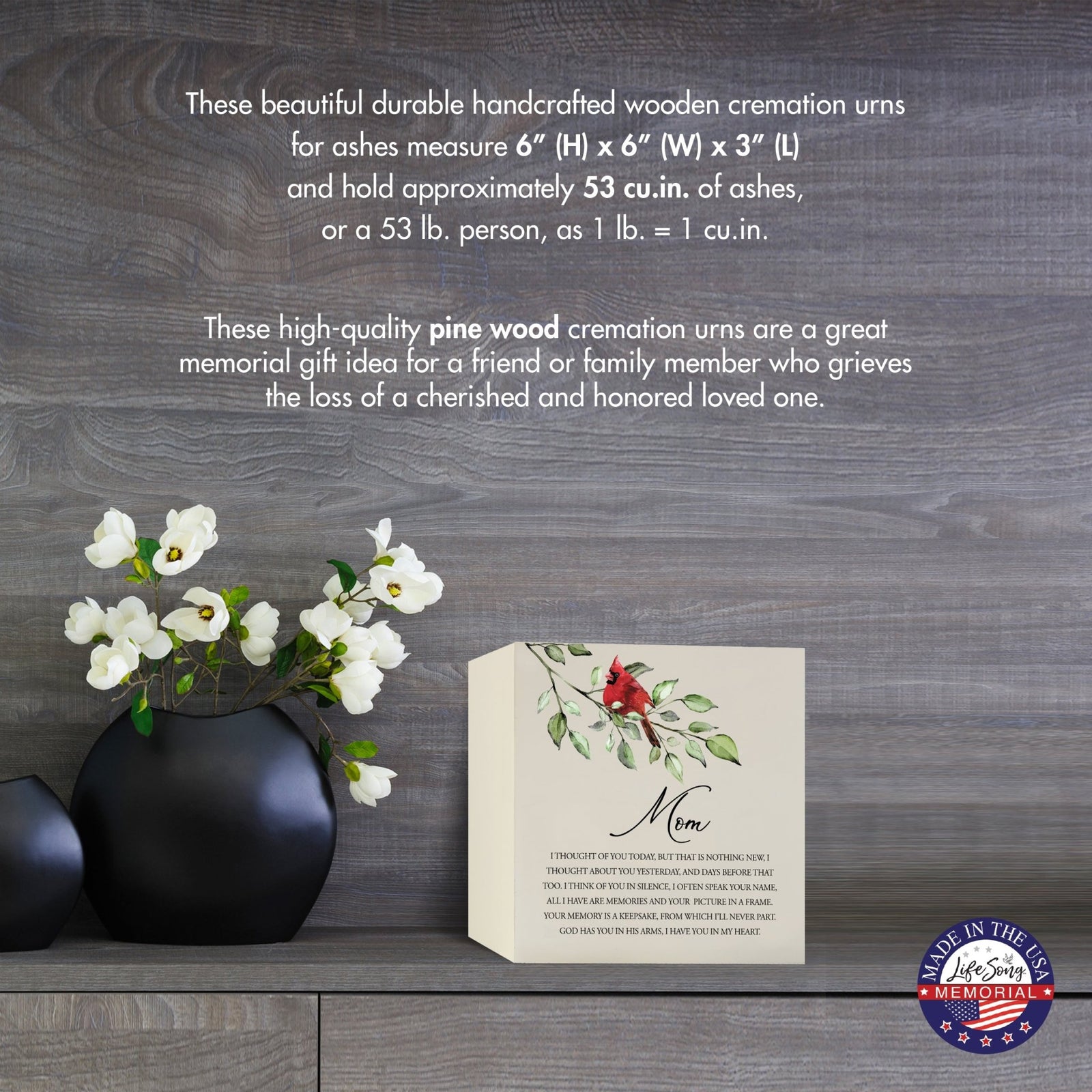 Cream-colored wooden shadow box urn for human ashes, measuring 6" x 6" x 3". The urn features a red cardinal and delicate floral design. Displayed on a wooden surface beside modern black vases with white flowers, this handcrafted urn is ideal for honoring adult loved ones.