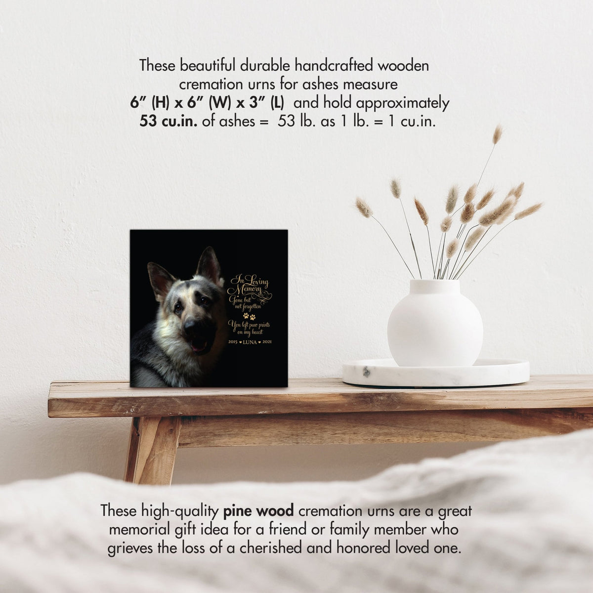 A wooden pet urn with size details, highlighting its handcrafted design with a white vase of pampas grass.