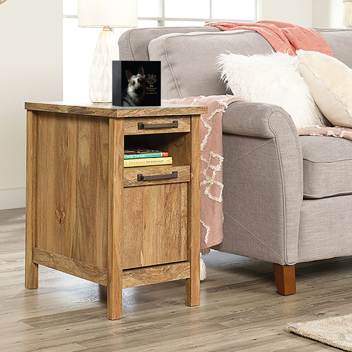 A personalized pet urn placed on a wooden side table beside a cozy gray couch.