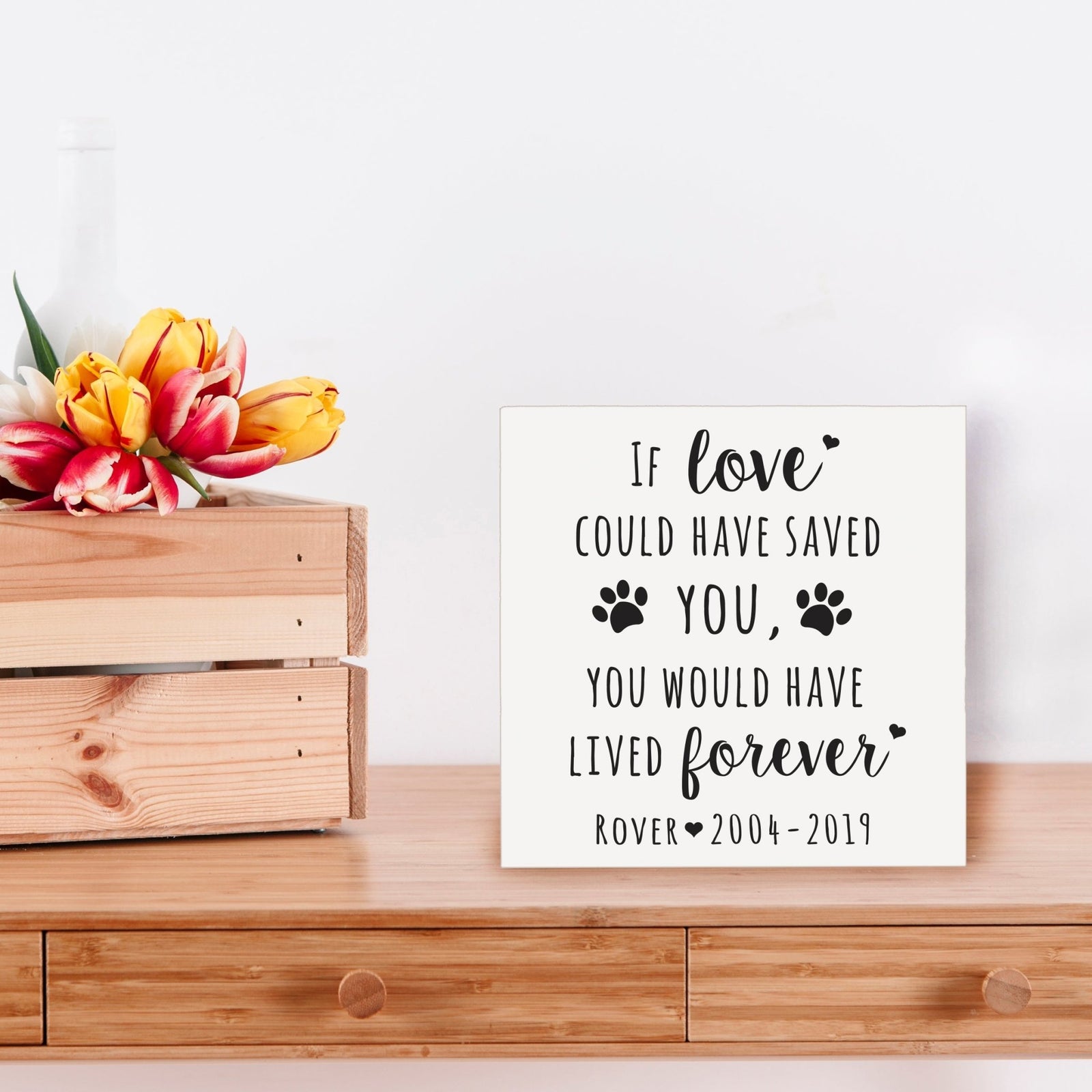 Black Lifesong Milestones Memorial Shadow Box Urn For Pet Ashes placed on a wooden table with a decorative setting, offering a meaningful way to honor a cherished dog or cat with an engraved sentimental quote.
