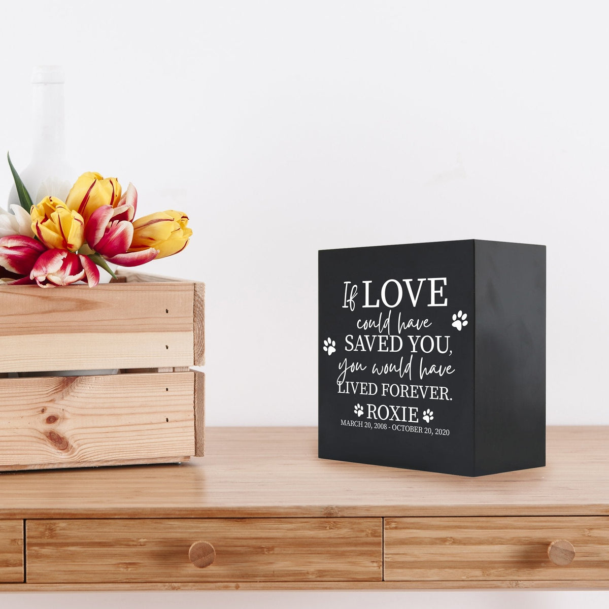 Black Lifesong Milestones Memorial Shadow Box Urn For Pet Ashes placed on a wooden table with a decorative setting, offering a meaningful way to honor a cherished dog or cat with an engraved sentimental quote.