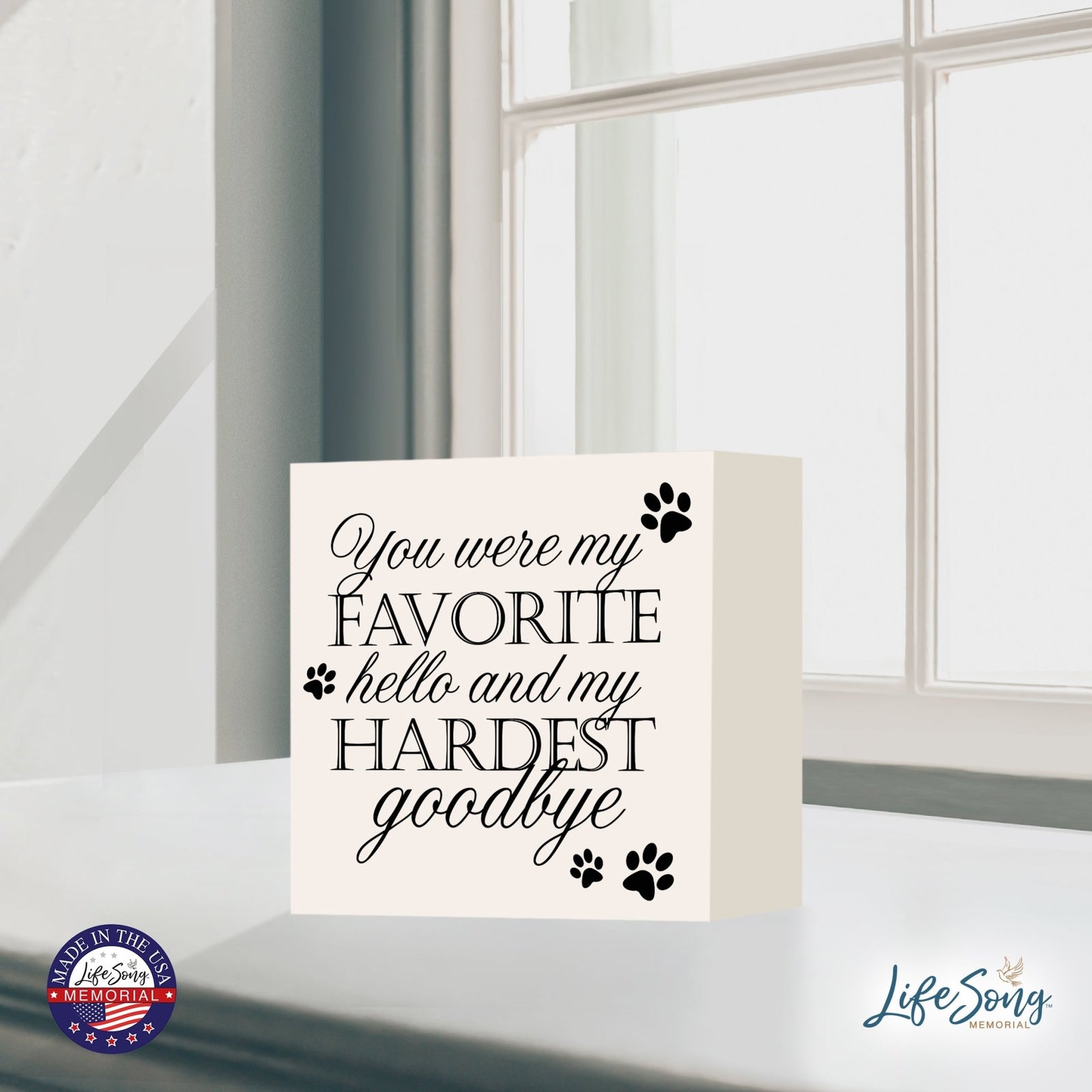 A cream-colored Lifesong Milestones Memorial Shadow Box Urn For Pet Ashes positioned near a window with soft natural light. The urn bears an elegant inscription, surrounded by paw prints, making it a beautiful pet memorial.