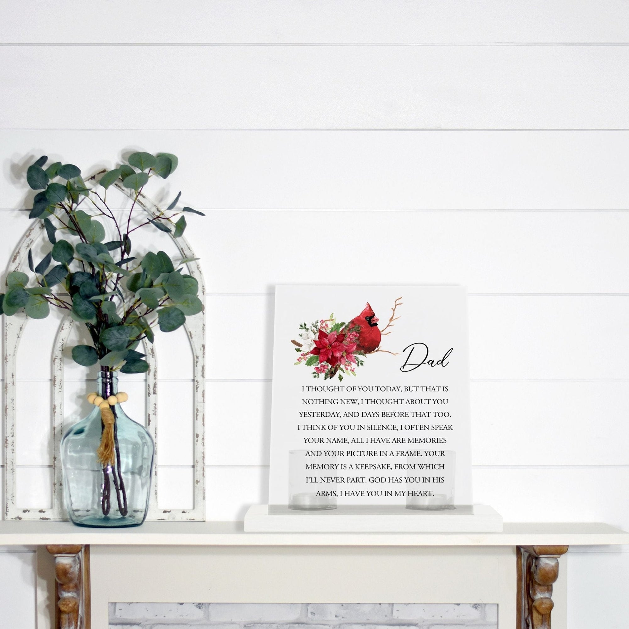 A solemn memorial display featuring a Lifesong Milestones Cardinal Memorial Frosted Acrylic Sign with Base and Votive Candle Holder. The tealight candle holder provides a warm glow, while votive candles surround it, creating a touching memory.