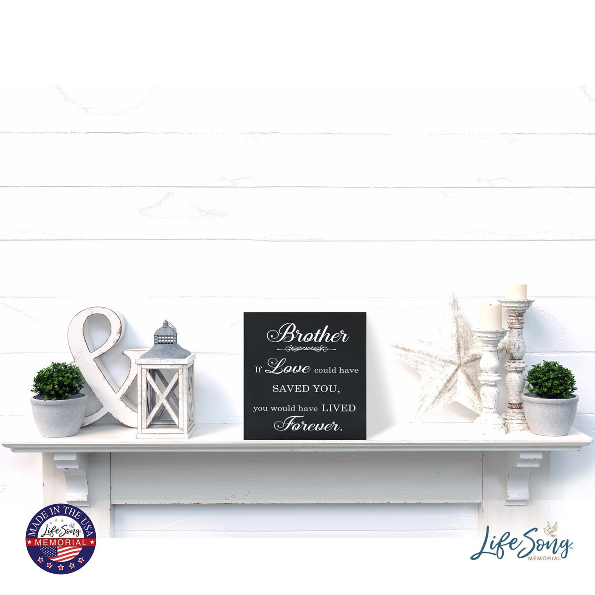 A decorative white shelf showcases a LifeSong Milestones Memorial Shadow Box Urn for human ashes, adorned with delightful accents such as lanterns, greenery, and star-shaped decorations. The urn features heartfelt engraving, fostering a serene and comforting ambiance.