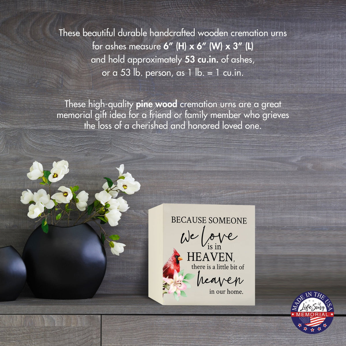 Cream-colored wooden shadow box urn for human ashes, measuring 6" x 6" x 3". The urn features a red cardinal and delicate floral design. Displayed on a wooden surface beside modern black vases with white flowers, this handcrafted urn is ideal for honoring adult loved ones.
