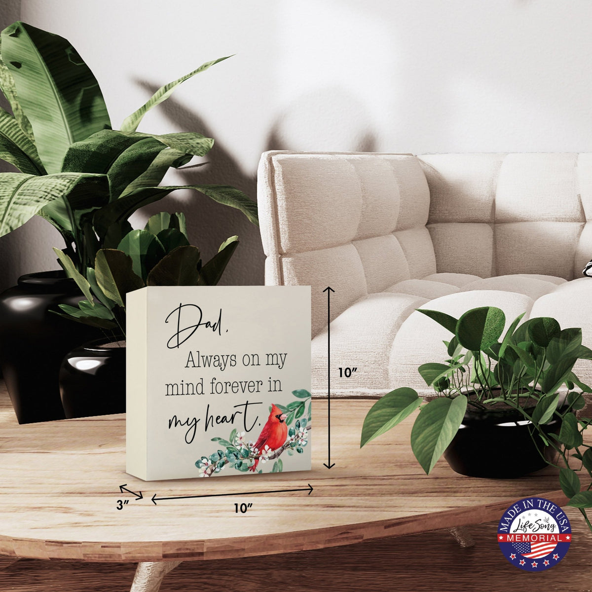 Modern wooden shadow box urn for human ashes, showcased on a minimalist wooden coffee table. This memorial urn, adorned with a cardinal and floral design, blends seamlessly with lush green indoor plants and cozy, contemporary furniture, making it an ideal keepsake for adult ashes.