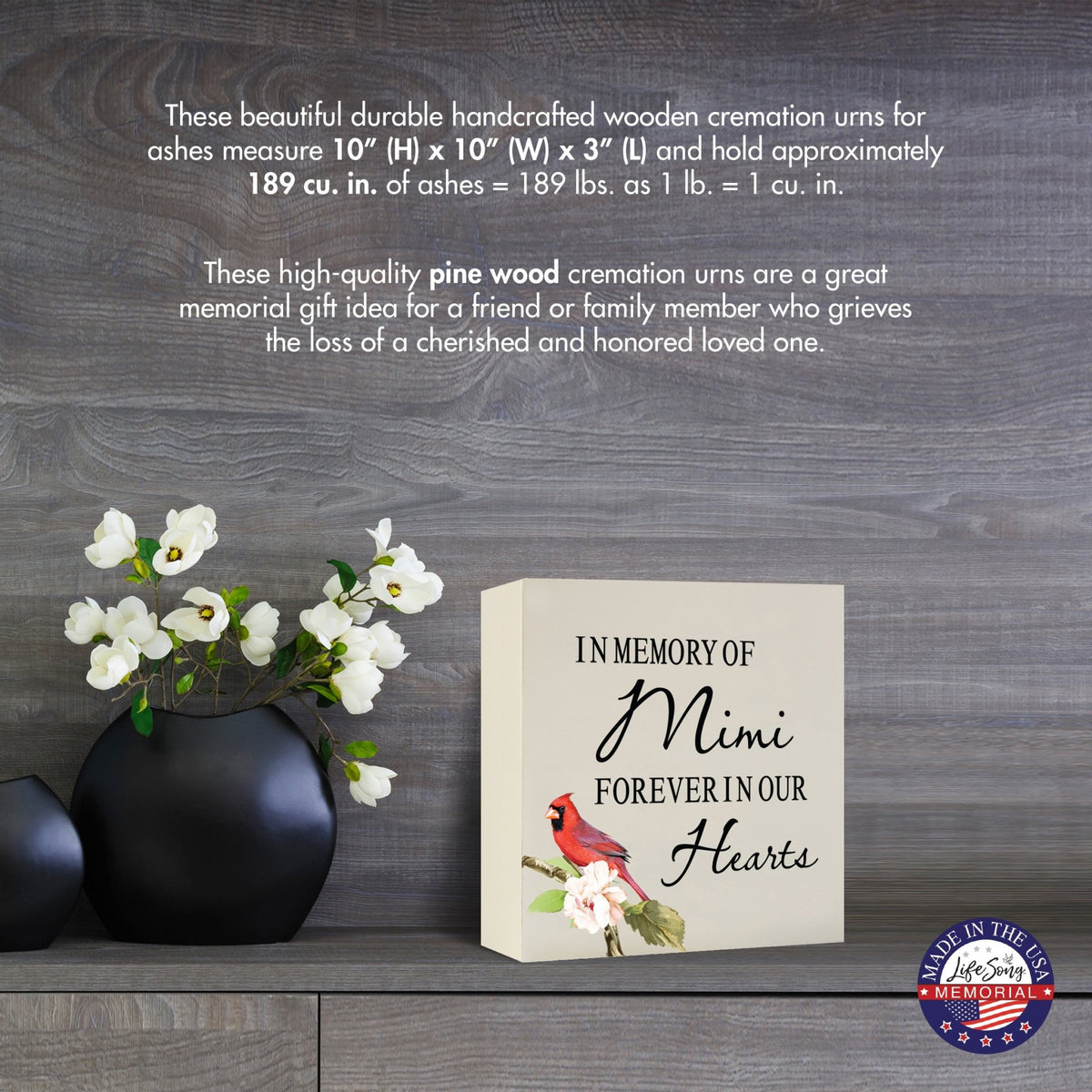 Cream-colored wooden shadow box urn for human ashes, measuring 6" x 6" x 3". The urn features a red cardinal and delicate floral design. Displayed on a wooden surface beside modern black vases with white flowers, this handcrafted urn is ideal for honoring adult loved ones.