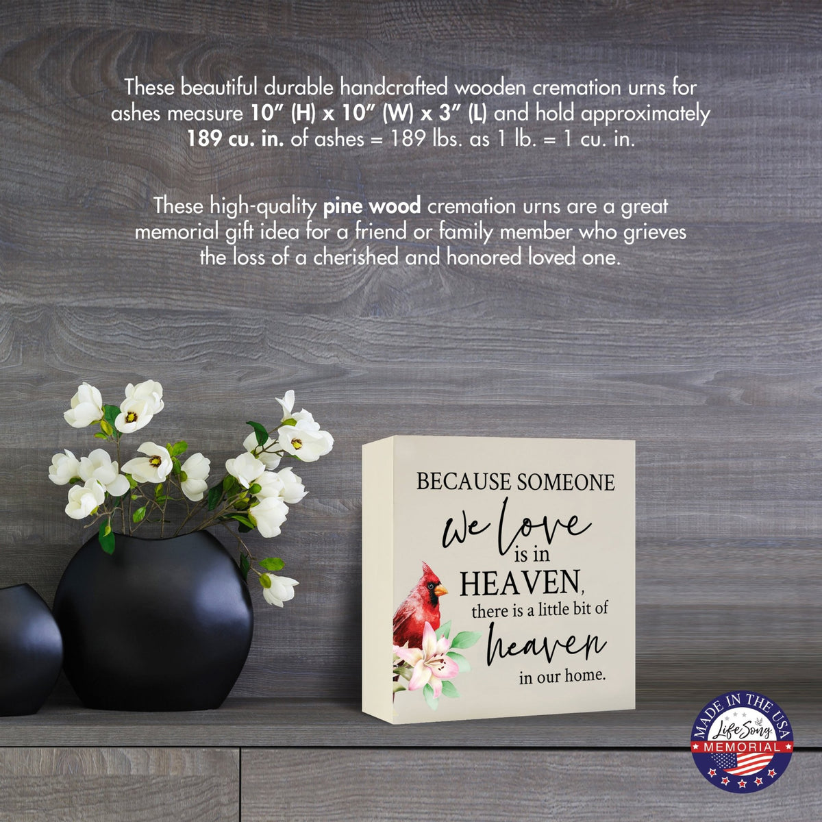 Cream-colored wooden shadow box urn for human ashes, measuring 6" x 6" x 3". The urn features a red cardinal and delicate floral design. Displayed on a wooden surface beside modern black vases with white flowers, this handcrafted urn is ideal for honoring adult loved ones.