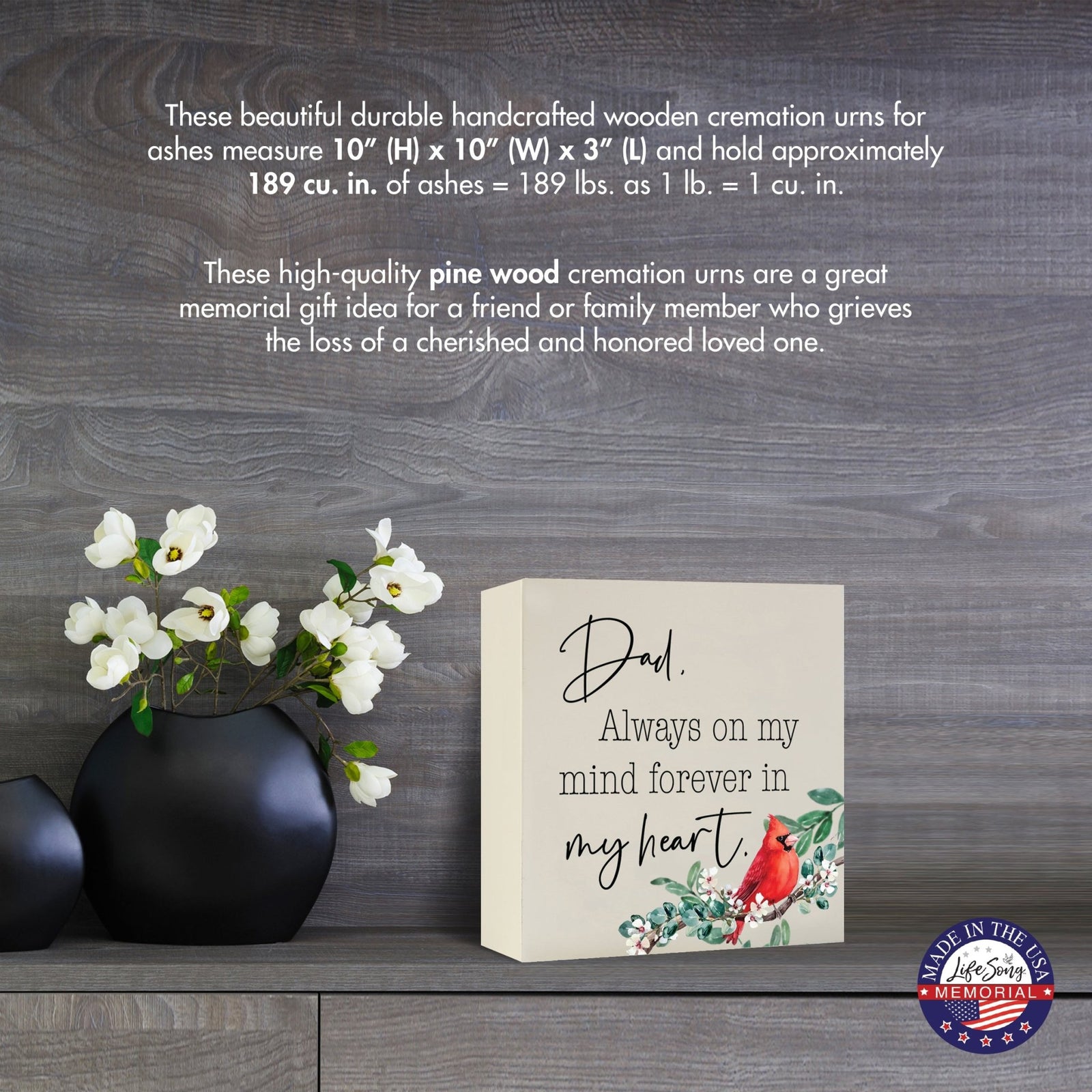 Cream-colored wooden shadow box urn for human ashes, measuring 6" x 6" x 3". The urn features a red cardinal and delicate floral design. Displayed on a wooden surface beside modern black vases with white flowers, this handcrafted urn is ideal for honoring adult loved ones.