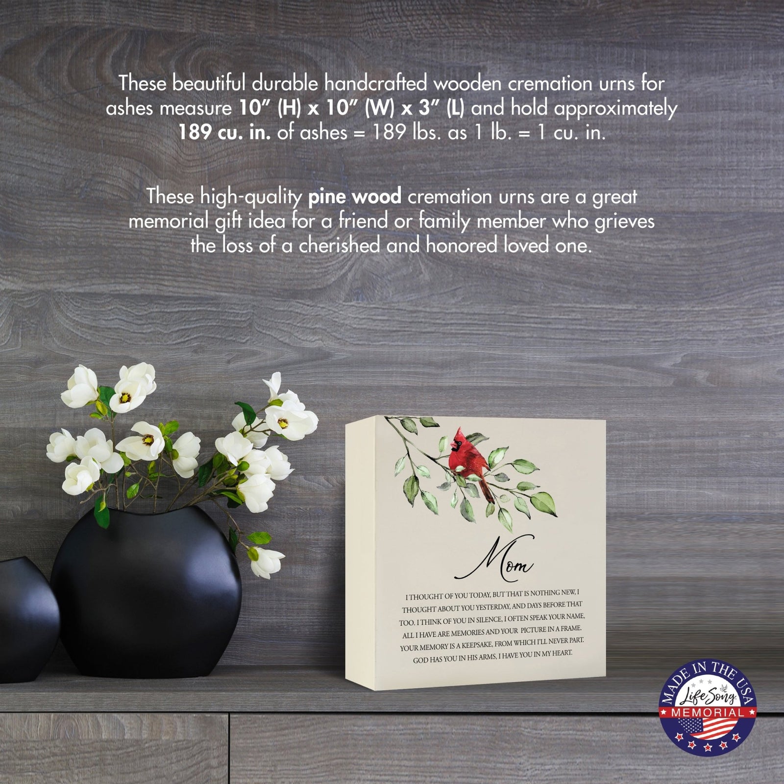 Cream-colored wooden shadow box urn for human ashes, measuring 6" x 6" x 3". The urn features a red cardinal and delicate floral design. Displayed on a wooden surface beside modern black vases with white flowers, this handcrafted urn is ideal for honoring adult loved ones.