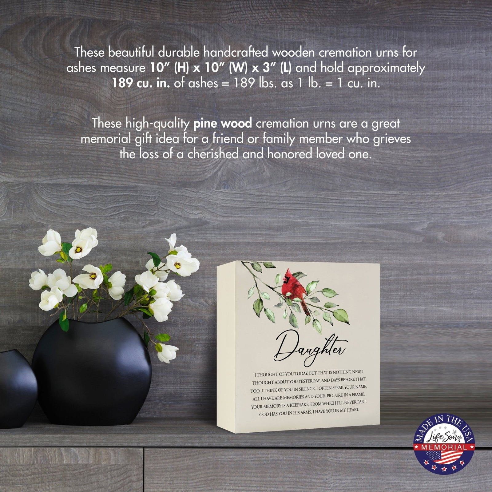 Cream-colored wooden shadow box urn for daughter, measuring 6" x 6" x 3". The urn features a red cardinal and delicate floral design. Displayed on a wooden surface beside modern black vases with white flowers, this handcrafted urn is ideal for honoring adult loved ones.