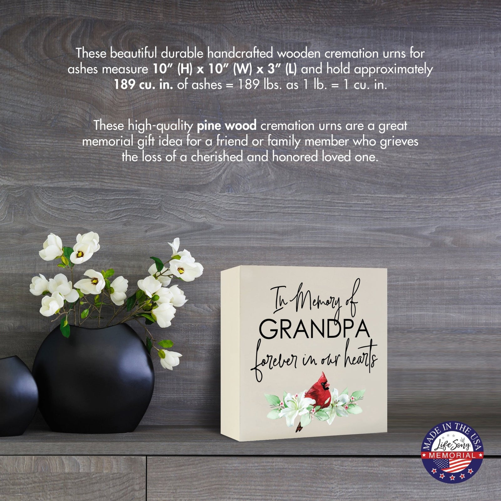 Cream-colored wooden shadow box urn for human ashes, measuring 6" x 6" x 3". The urn is inscribed with "In Memory of Grandpa - Forever in our hearts" alongside a red cardinal and delicate floral design. Displayed on a wooden surface beside modern black vases with white flowers, this handcrafted urn is ideal for honoring adult loved ones.